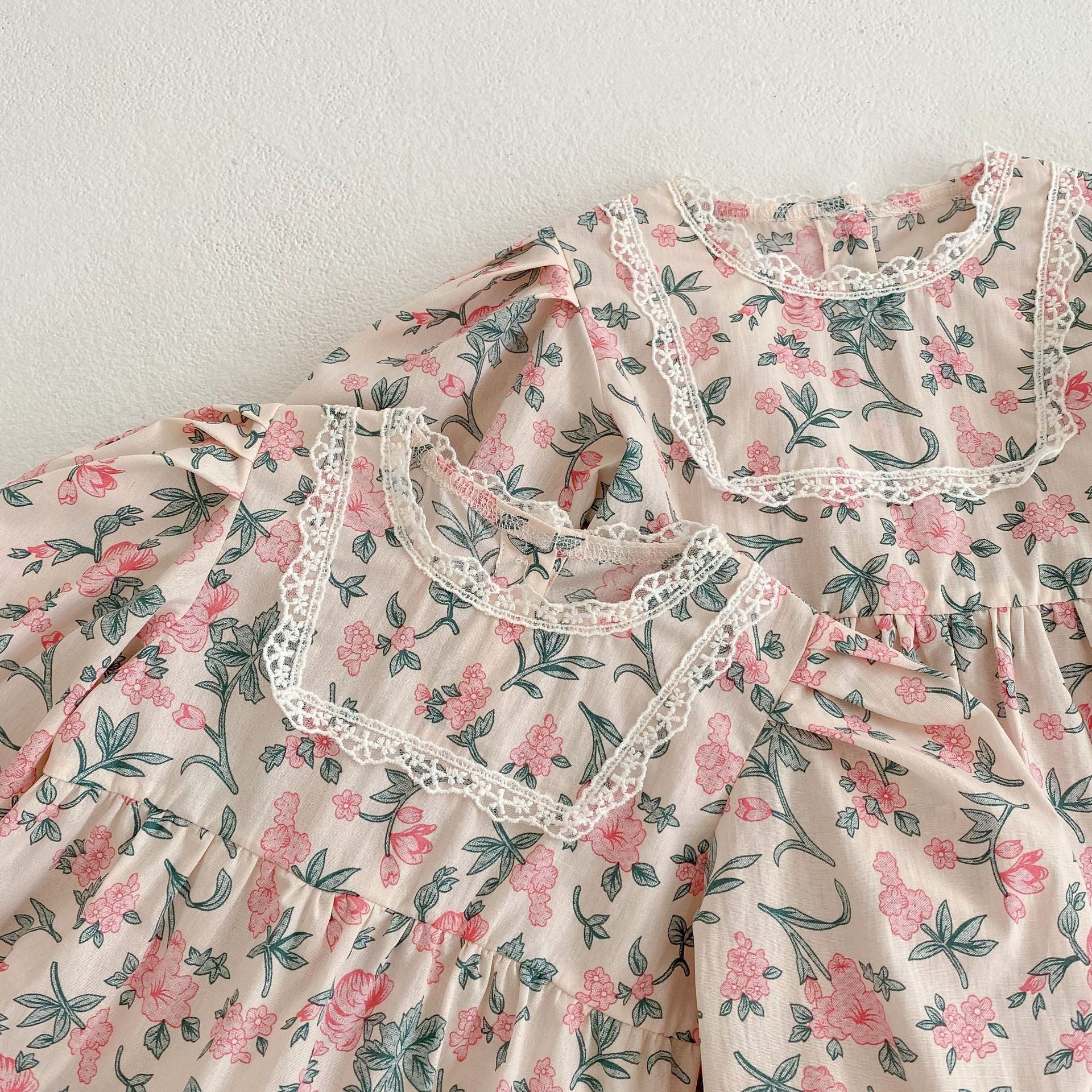 A cute baby girl wearing a floral print onesie and dress with mesh patchwork design in pink and light pink colors.