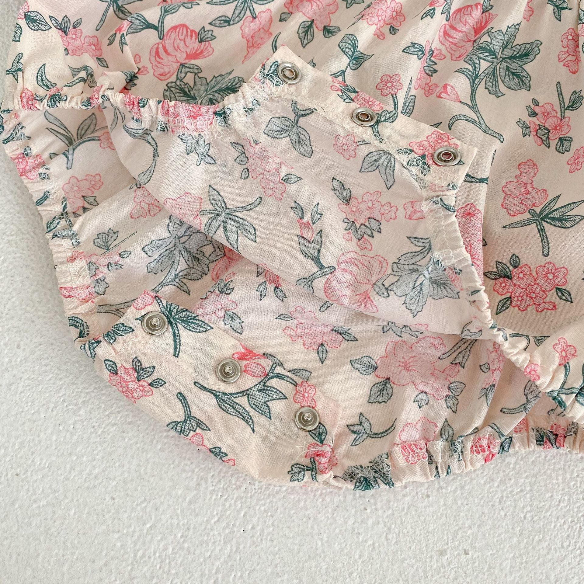 A cute baby girl wearing a floral print onesie and dress with mesh patchwork design in pink and light pink colors.