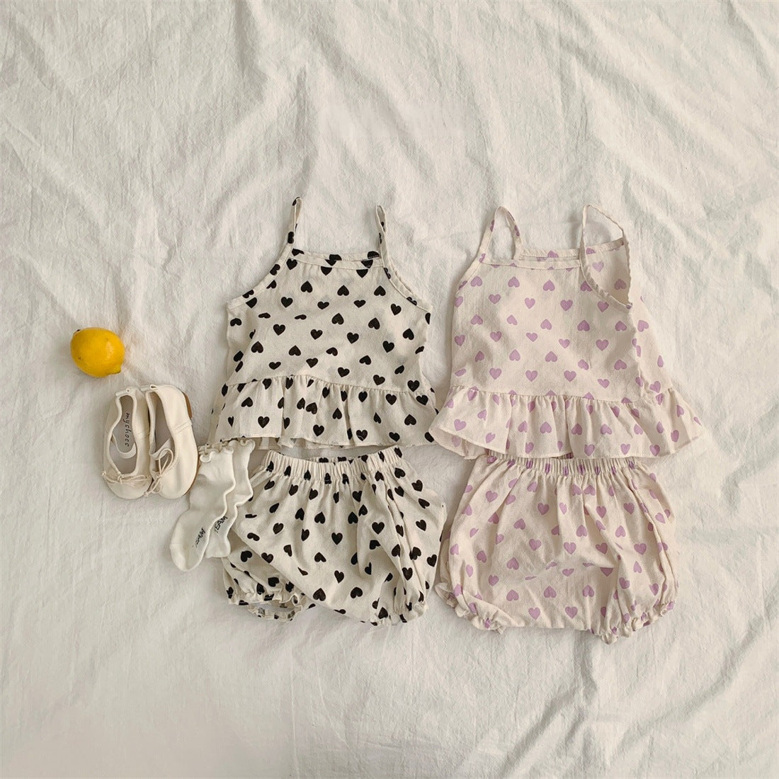 Baby girl wearing a heart pattern sling top with matching shoers, showcasing a cute summer outfit in black and pink.