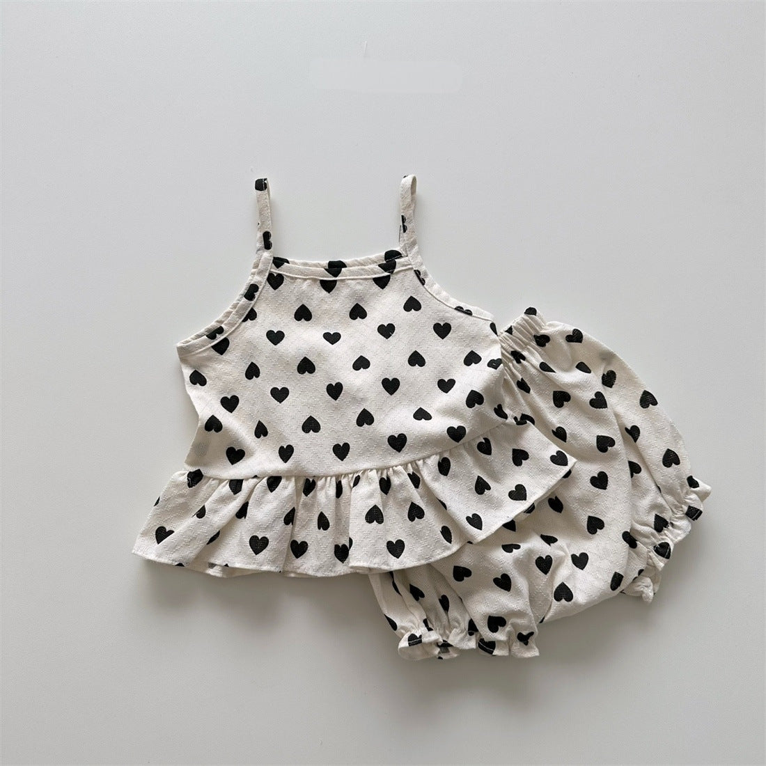 Baby girl wearing a heart pattern sling top with matching shoers, showcasing a cute summer outfit in black and pink.