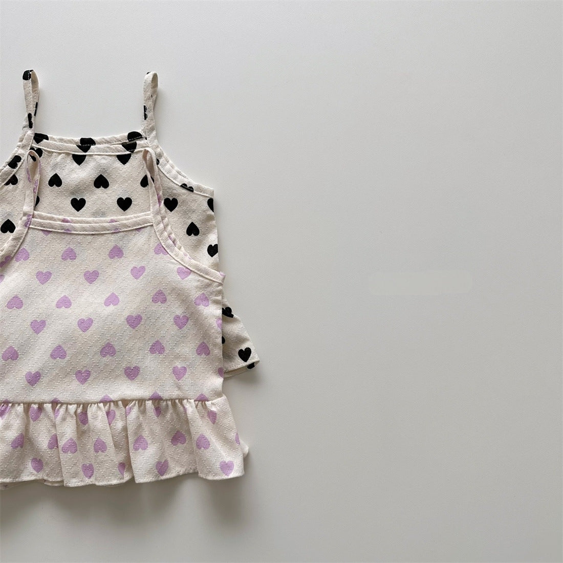 Baby girl wearing a heart pattern sling top with matching shoers, showcasing a cute summer outfit in black and pink.