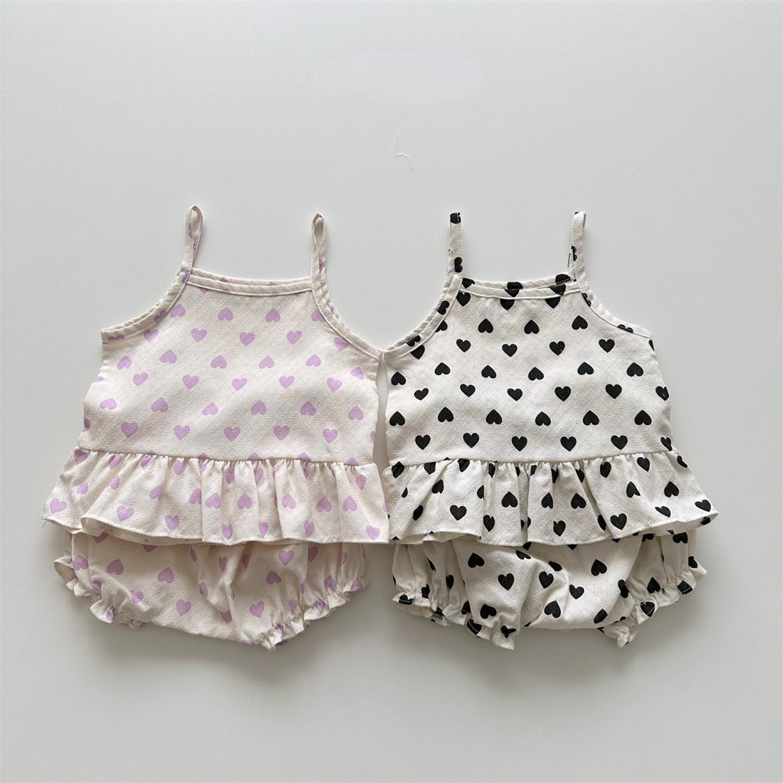 Baby girl wearing a heart pattern sling top with matching shoers, showcasing a cute summer outfit in black and pink.