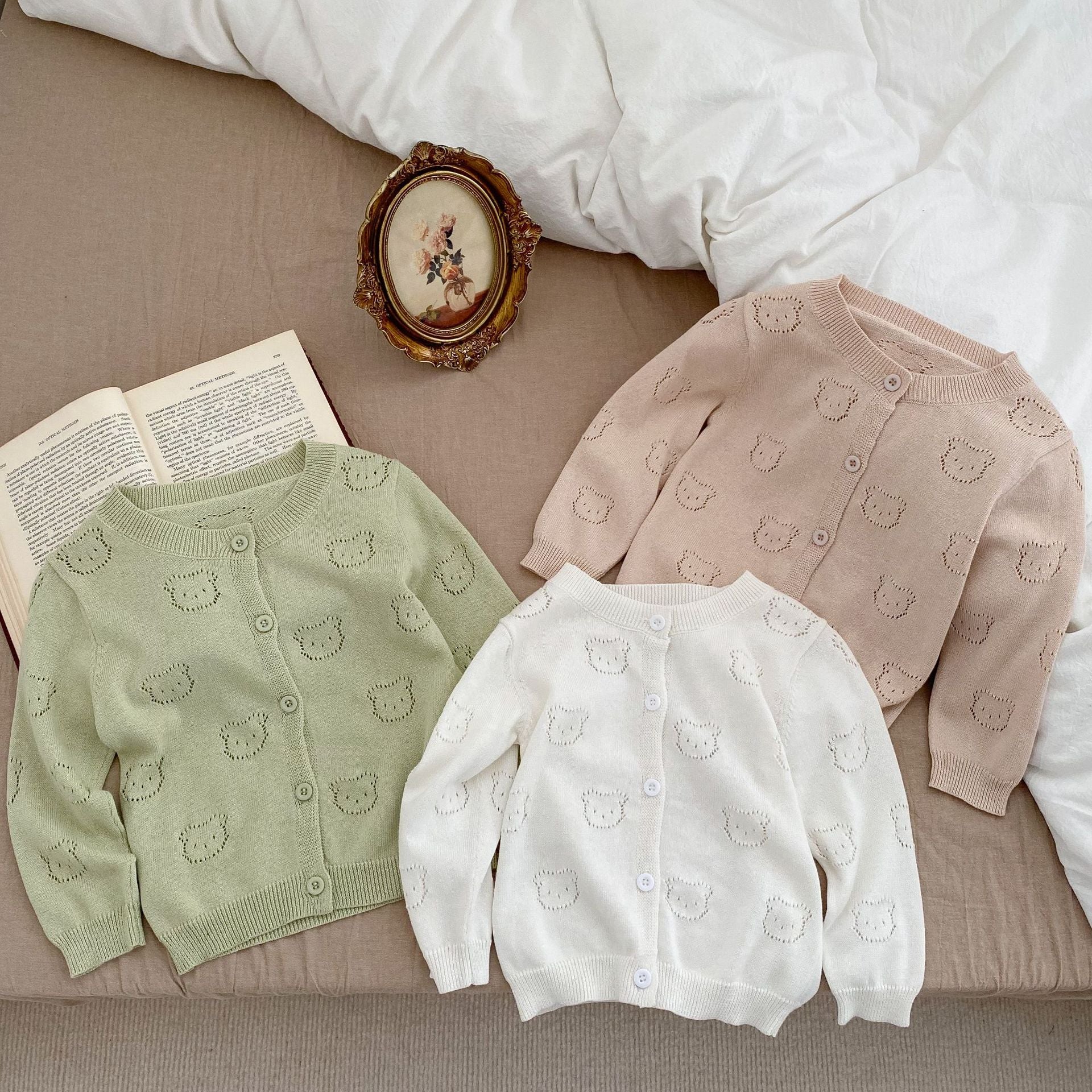 A soft cotton cardigan for baby girls featuring a hollow carved design, available in white, pink, and green.