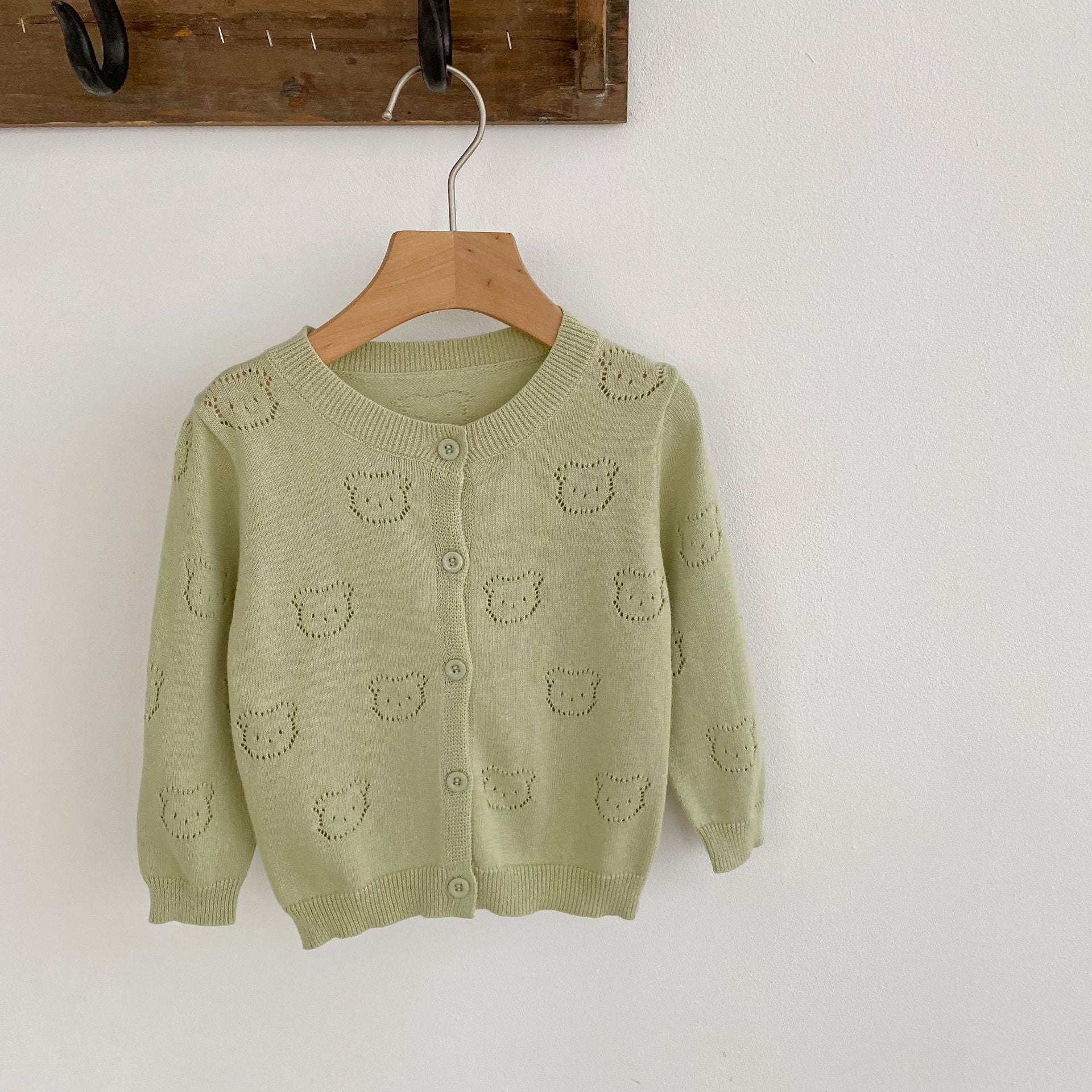 A soft cotton cardigan for baby girls featuring a hollow carved design, available in white, pink, and green.