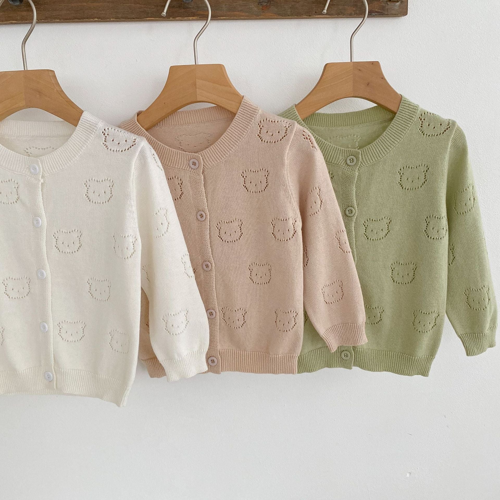A soft cotton cardigan for baby girls featuring a hollow carved design, available in white, pink, and green.