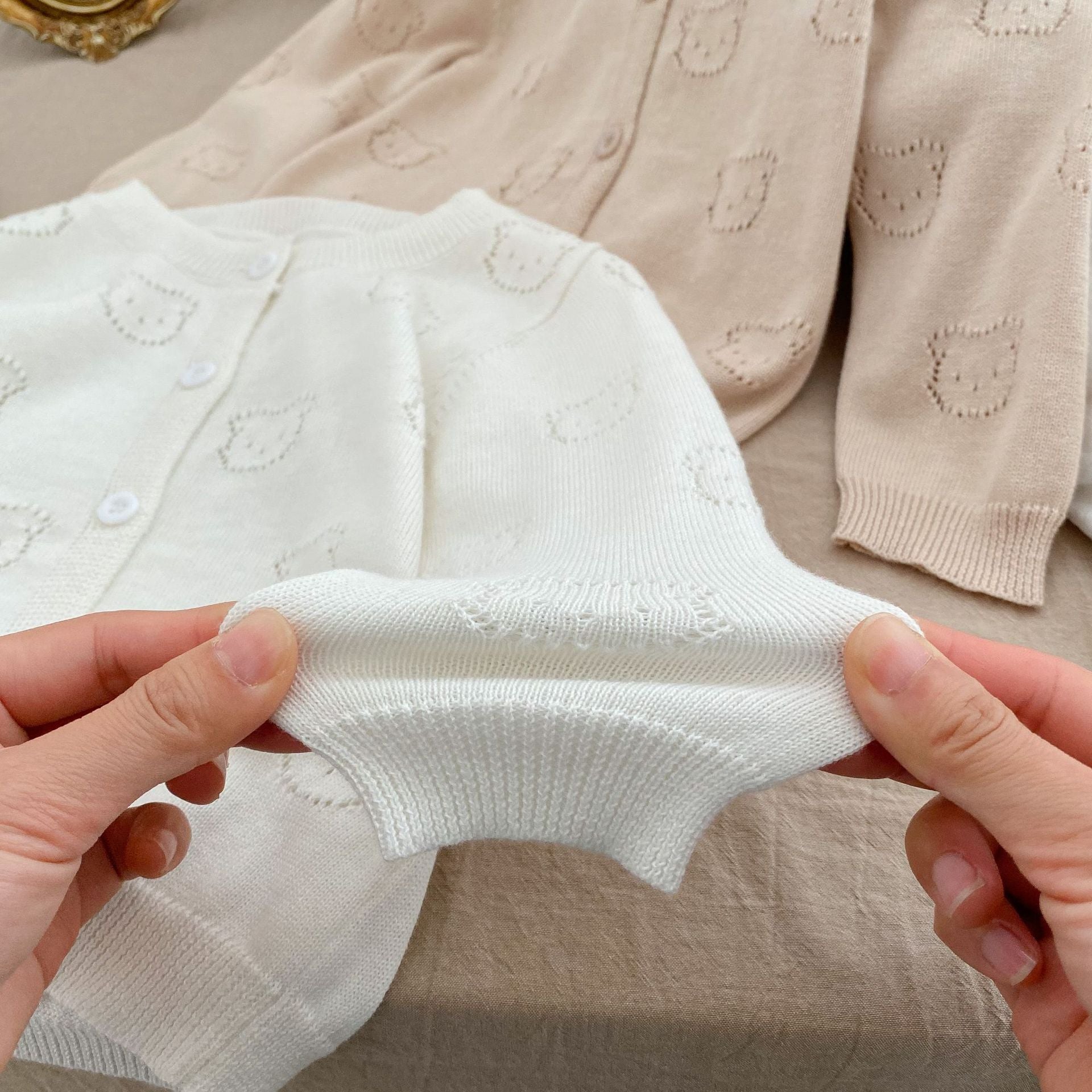 A soft cotton cardigan for baby girls featuring a hollow carved design, available in white, pink, and green.