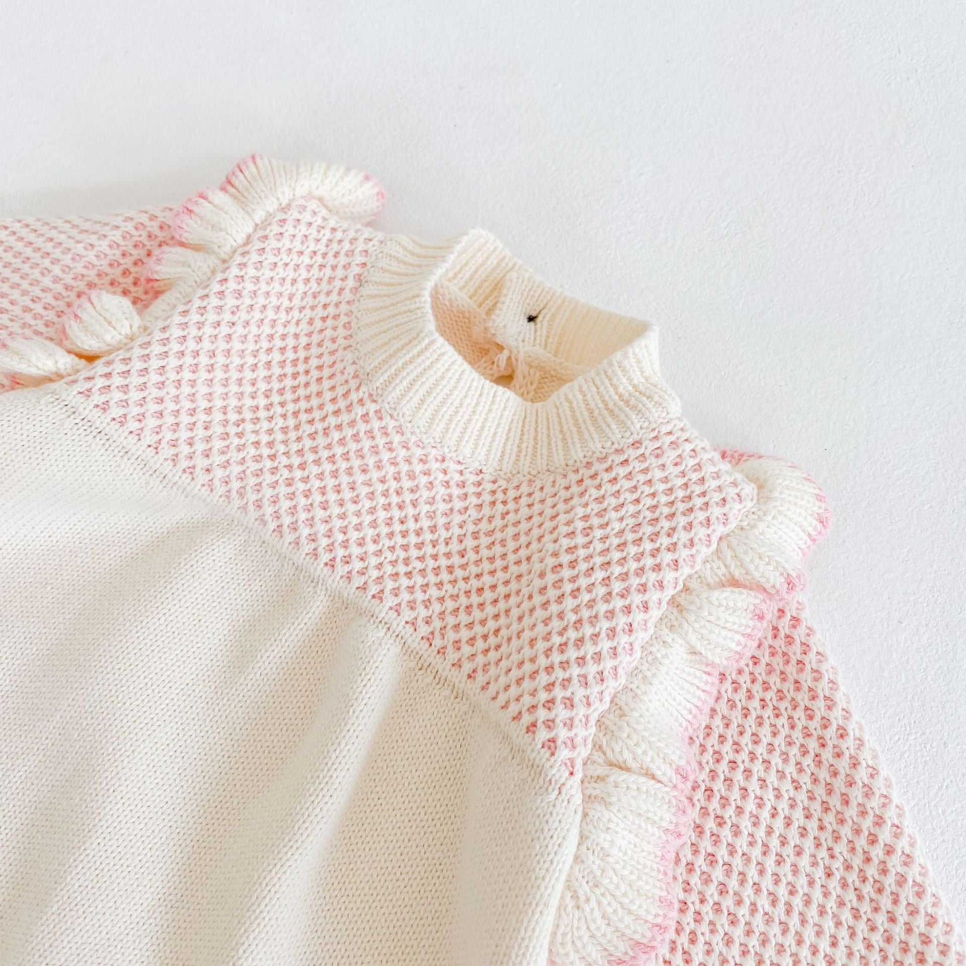 Baby girl knitted onesie in pink with ruffle design and contrast pattern, perfect for spring and autumn wear.