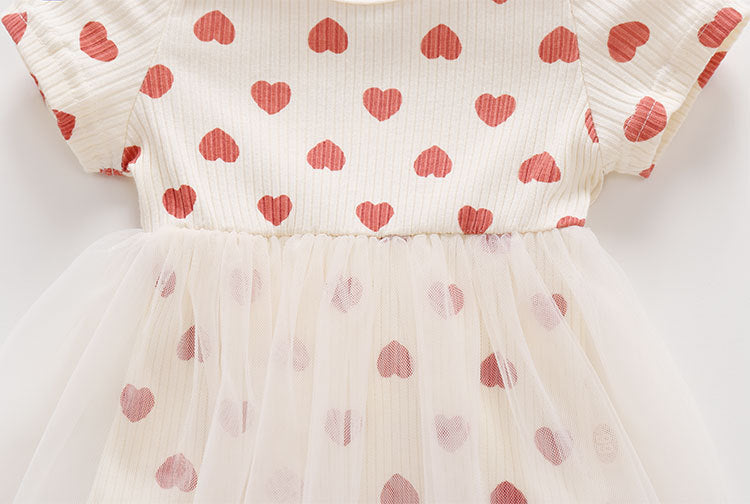 Baby girl onesie dress featuring mesh patchwork design and small heart print pattern in beige color.