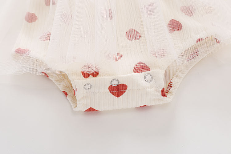 Baby girl onesie dress featuring mesh patchwork design and small heart print pattern in beige color.
