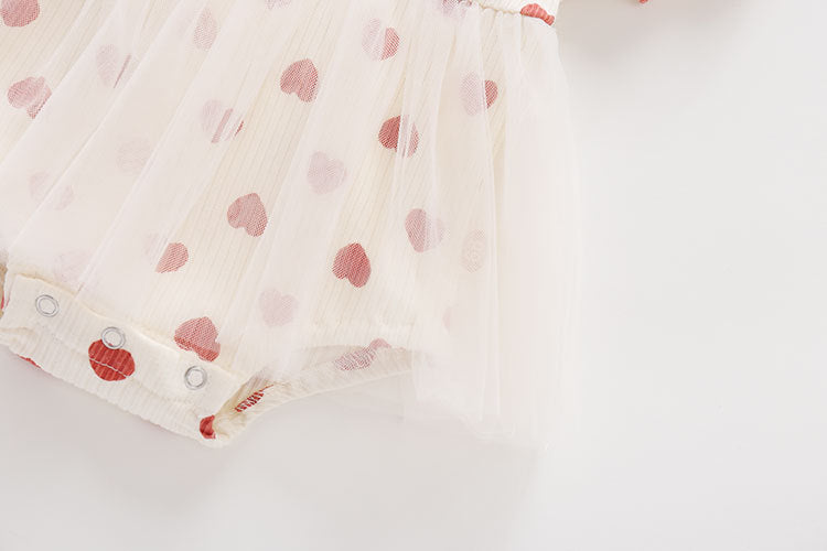 Baby girl onesie dress featuring mesh patchwork design and small heart print pattern in beige color.