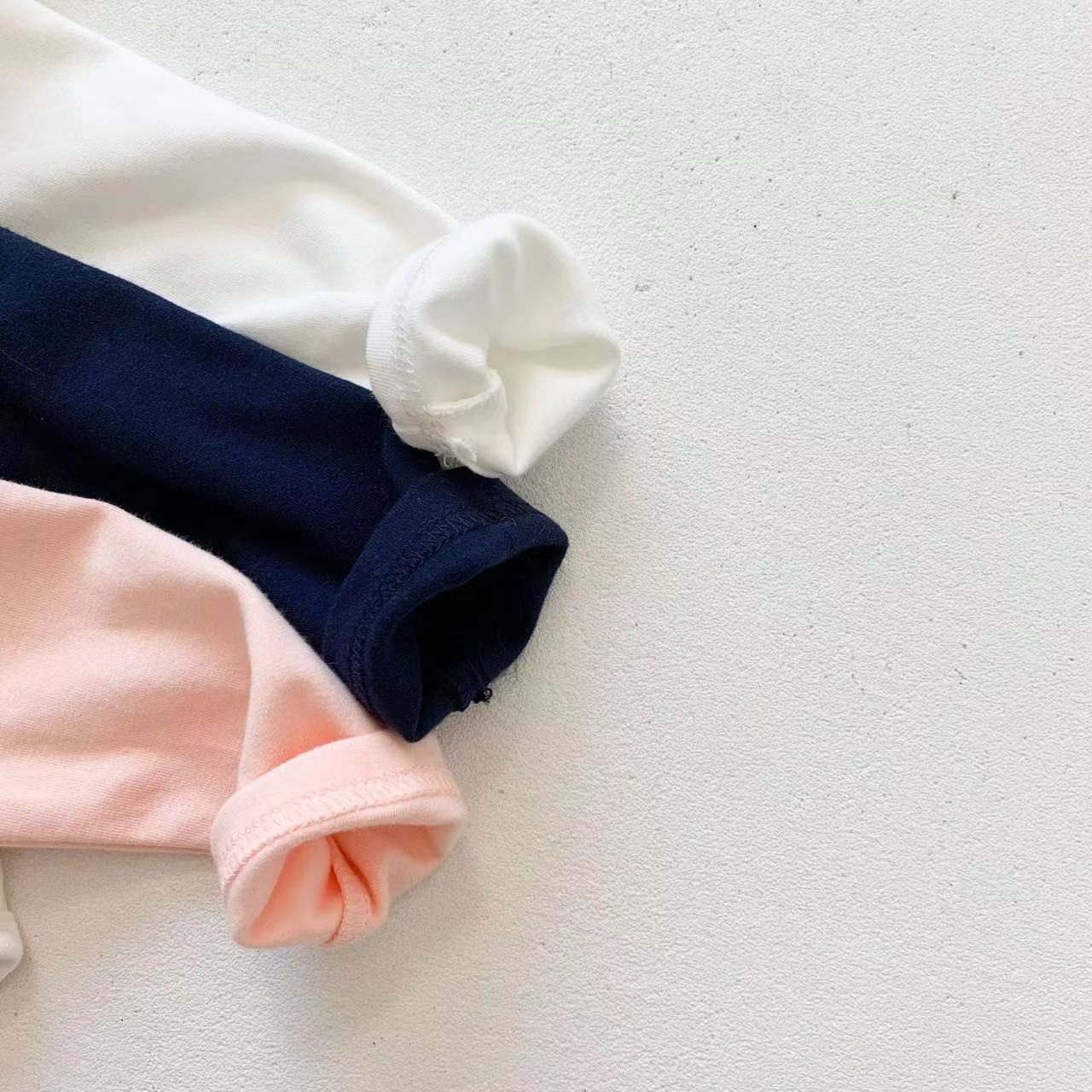 Adorable baby girl wearing a mesh ruffle neck long sleeved onesie in solid color, showcasing comfort and style.