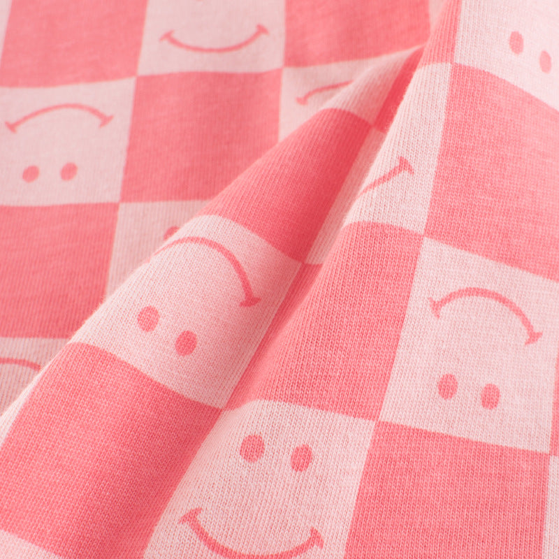Baby girl wearing a pink plaid pattern t-shirt with a smiley face print, perfect for summer outings.