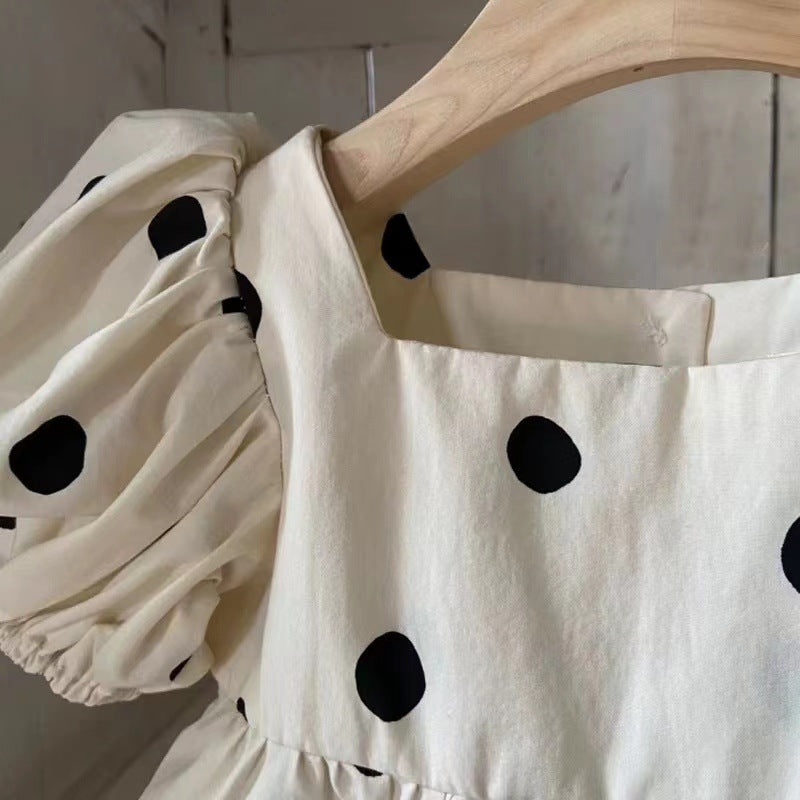 Baby girl wearing a polka dot pattern onesie with square collar and puff sleeves, showcasing a stylish summer outfit.