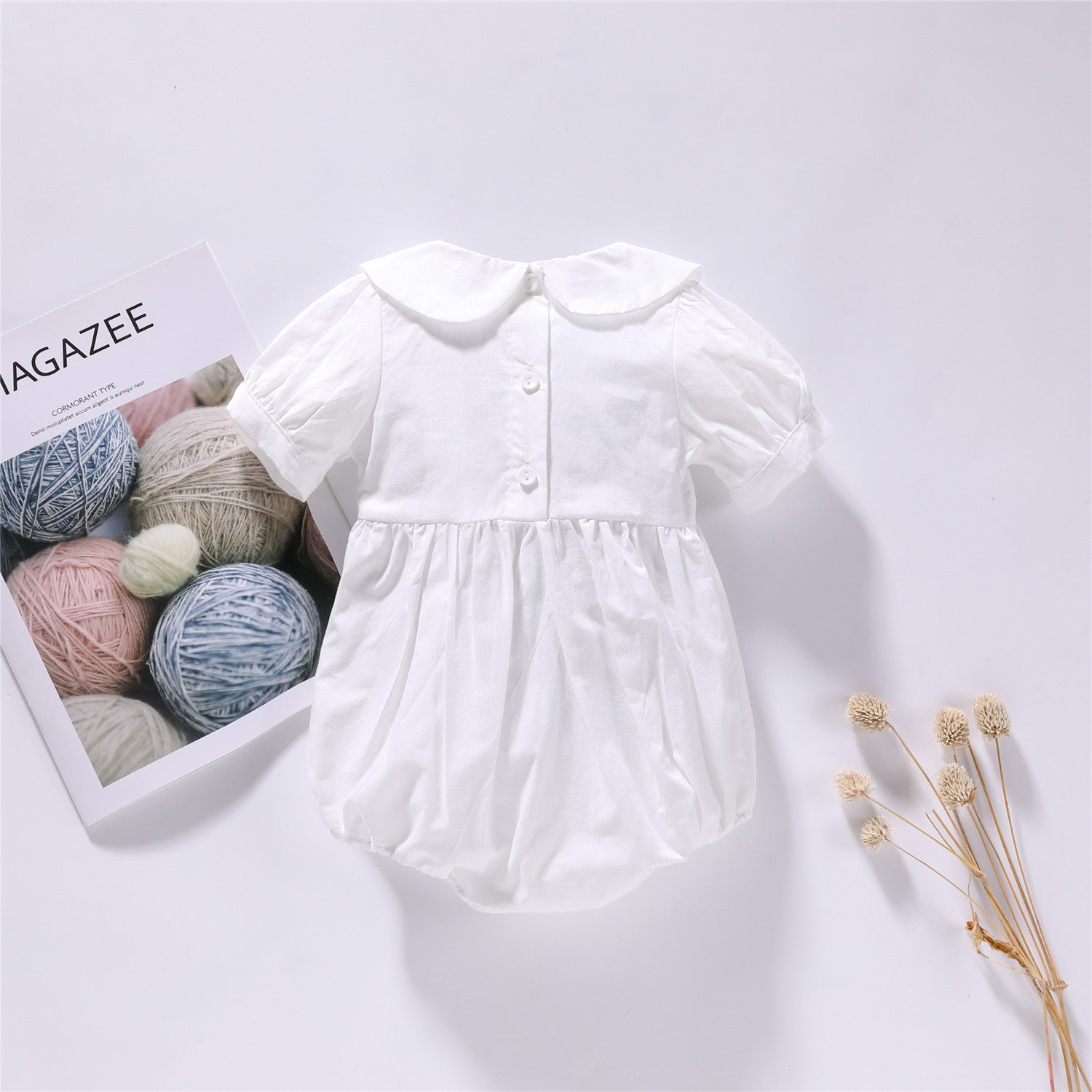 Baby girl onesie featuring cherry embroidery and puff sleeves in white and pink colors, made from soft cotton fabric.
