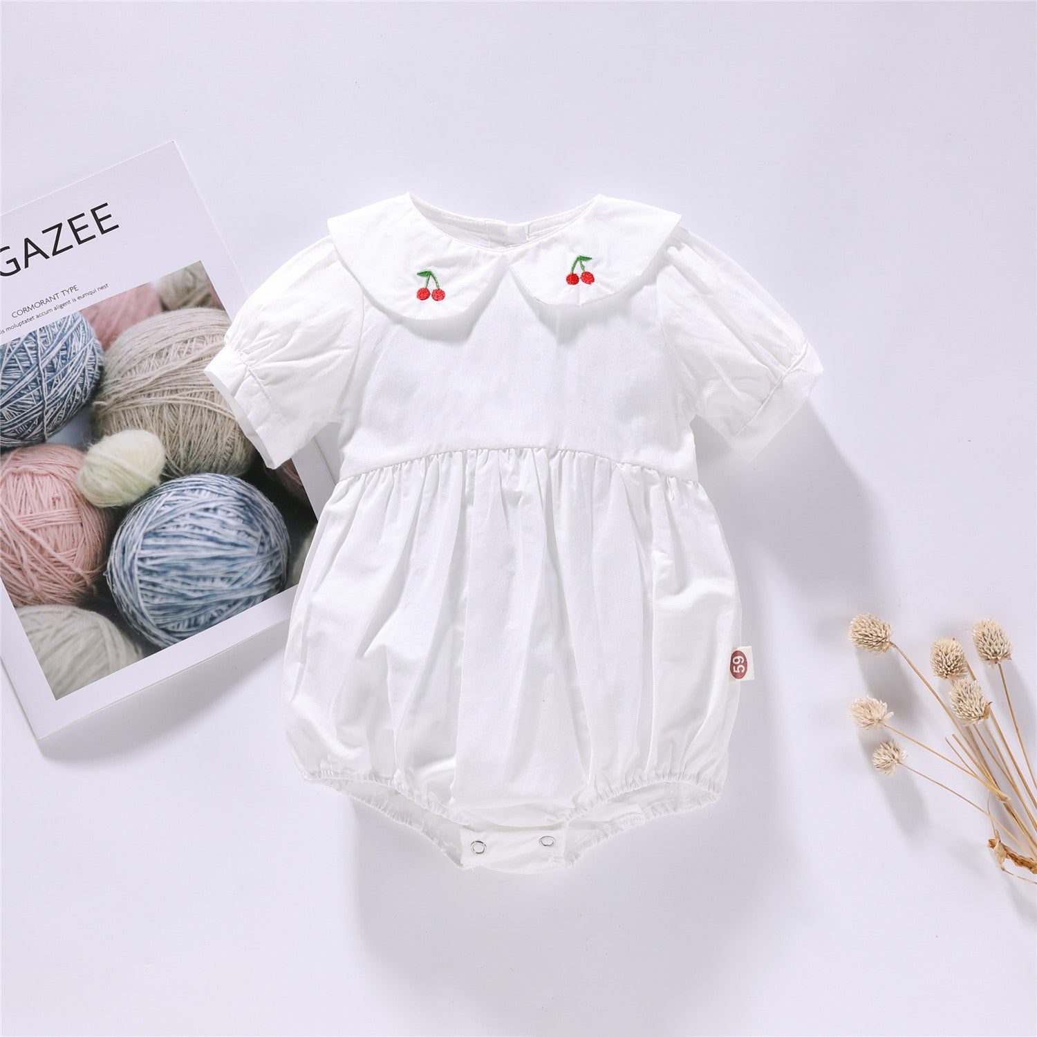 Baby girl onesie featuring cherry embroidery and puff sleeves in white and pink colors, made from soft cotton fabric.