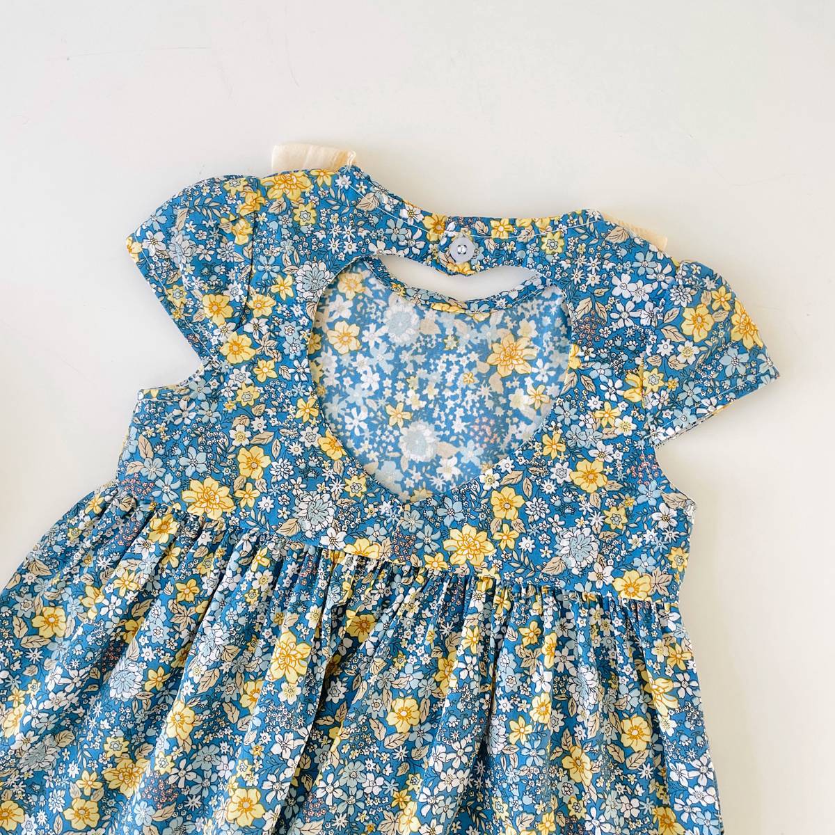 Baby girl wearing a floral print backless dress with a bow, showcasing a vibrant green color and doll-neck design.