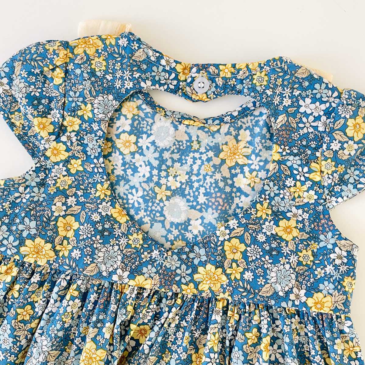 Baby girl wearing a floral print backless dress with a bow, showcasing a vibrant green color and doll-neck design.