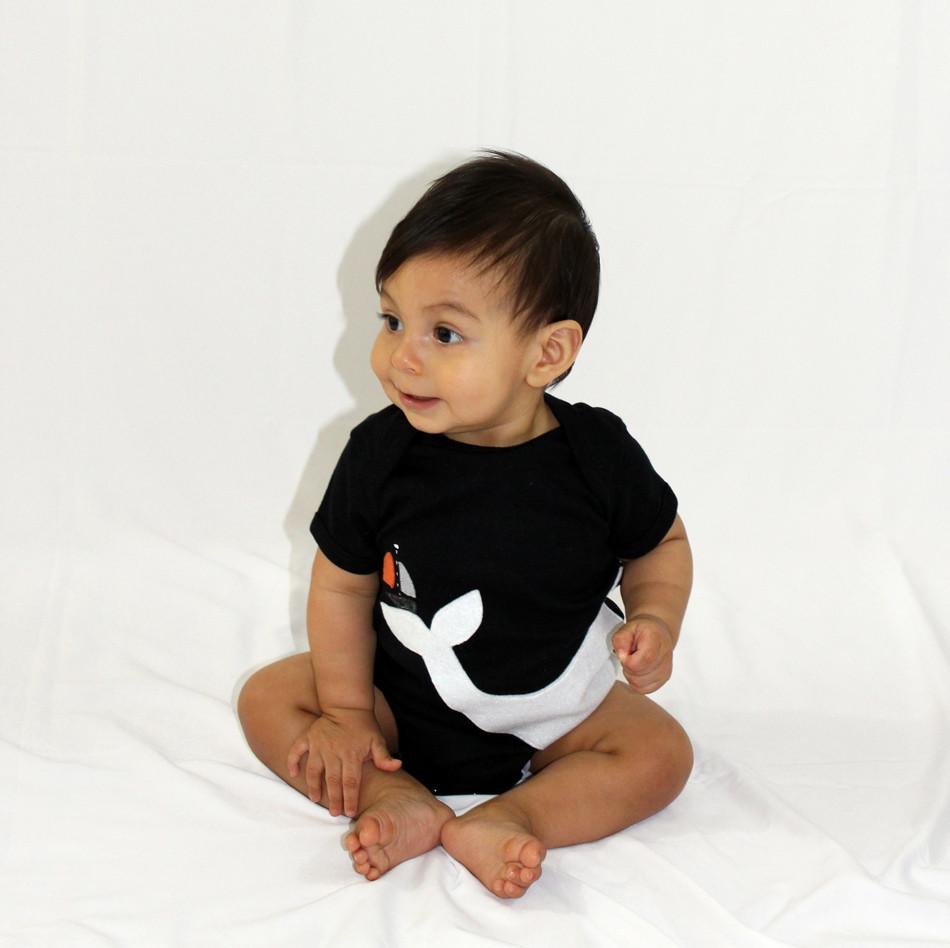 A handmade baby onesie featuring a big white whale and a little sailboat design on a black background, perfect for infants.