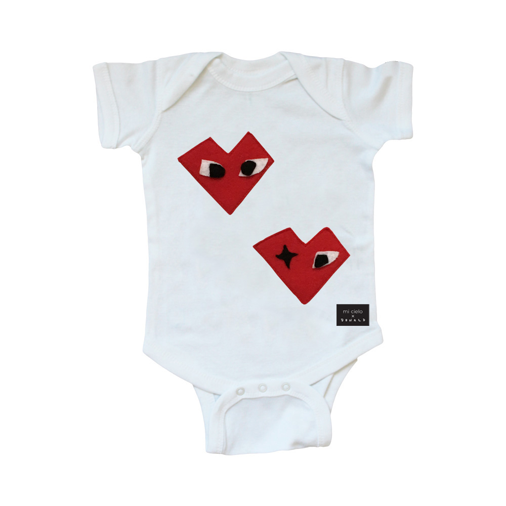 A white baby onesie featuring colorful felt appliqués designed by Donald Robertson, showcasing a heart motif, perfect for infants.