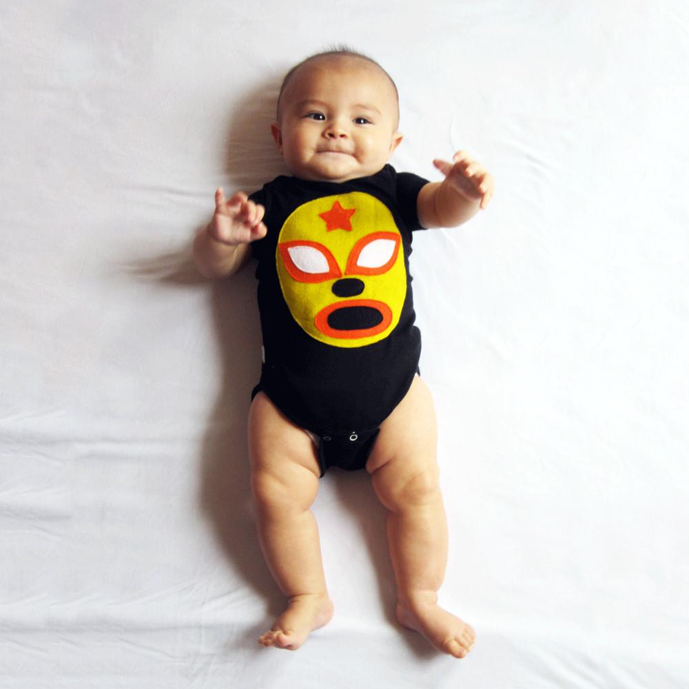 A vibrant yellow baby onesie featuring a luchador mask design, handmade with love and care, perfect for infants.
