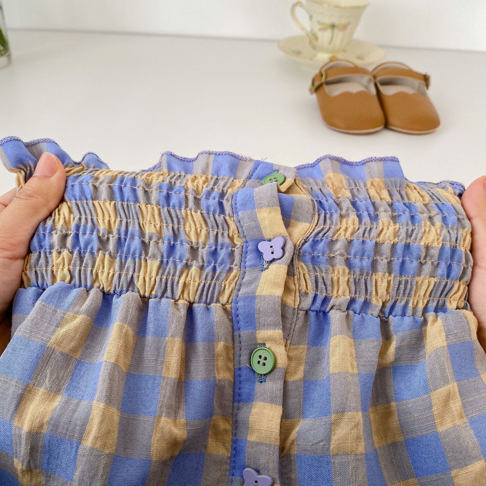Adorable baby girl wearing a blue plaid pattern sling blouse with matching shorts, perfect for summer outings.