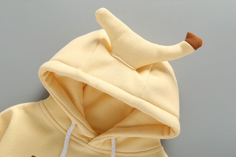 Baby girl wearing a yellow long-sleeved bodysuit with 3D banana patches and a matching hat, showcasing a playful slogan print.