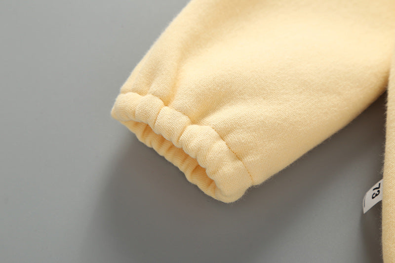 Baby girl wearing a yellow long-sleeved bodysuit with 3D banana patches and a matching hat, showcasing a playful slogan print.