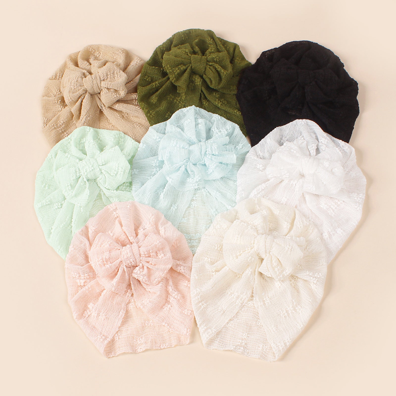 A collection of baby hats in solid colors including white, pink, blue, green, and beige, showcasing their elastic fit and breathable cotton material.