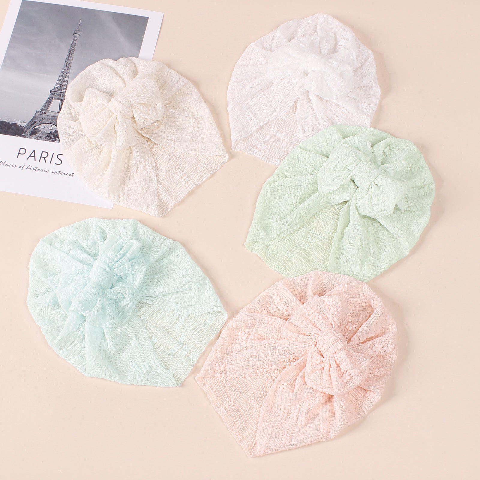 A collection of baby hats in solid colors including white, pink, blue, green, and beige, showcasing their elastic fit and breathable cotton material.