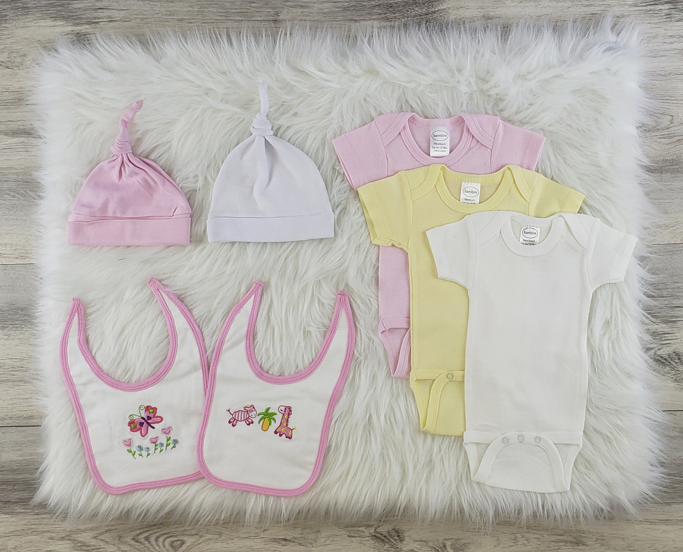 Bambini 7 Pc Layette Baby Clothes Set featuring soft cotton onesies, knotted caps, and bibs in pastel colors for newborns.