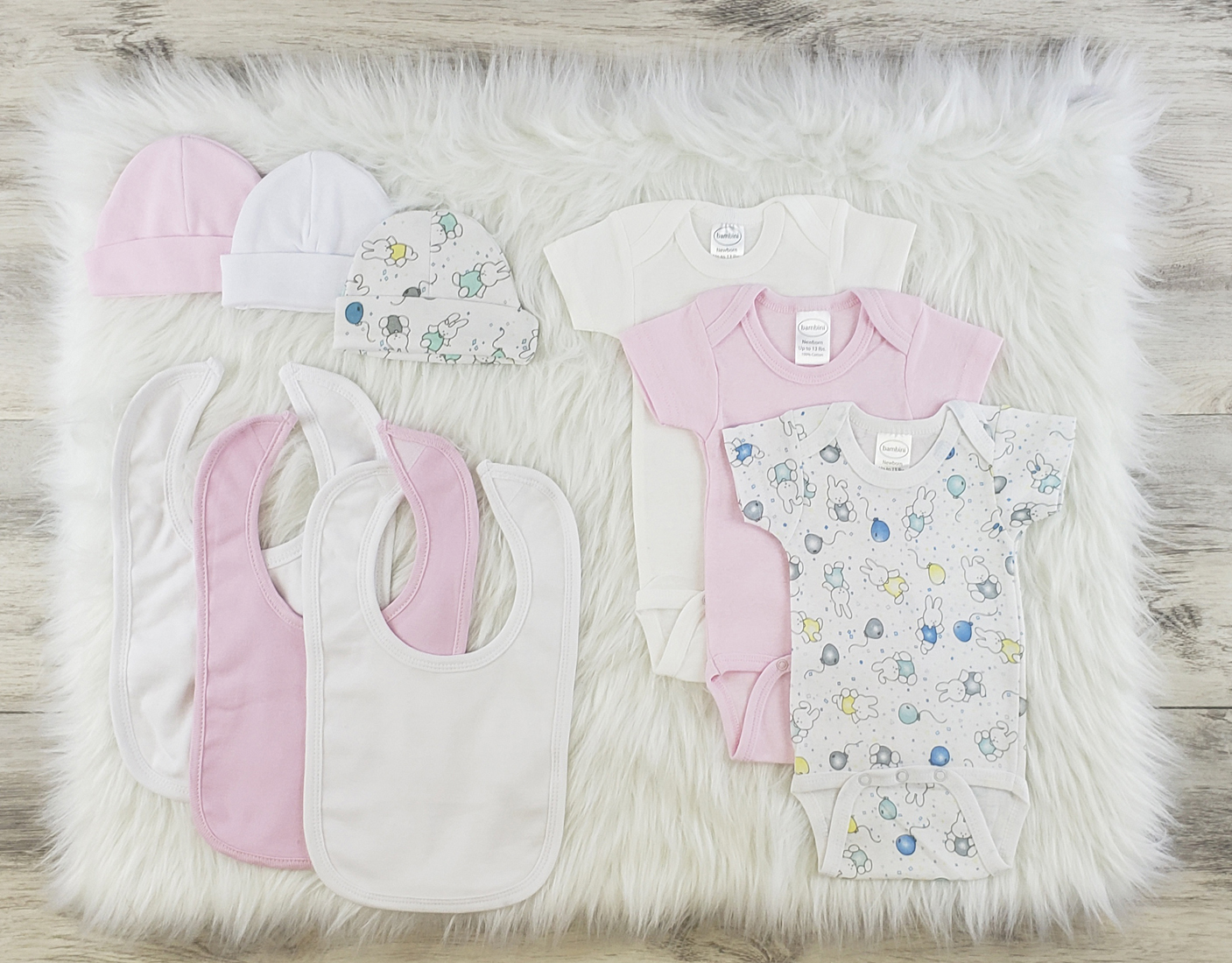 Bambini 9 Pc Layette Baby Clothes Set featuring soft cotton onesies, caps, and bibs in pink and white, perfect for newborns.