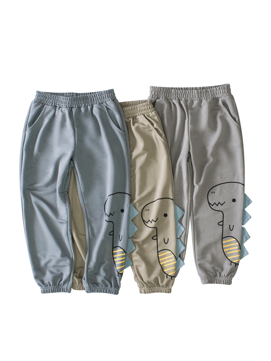 Children's boys sports trousers featuring a dinosaur cartoon design, available in blue, grey, and khaki colors, with functional pockets.