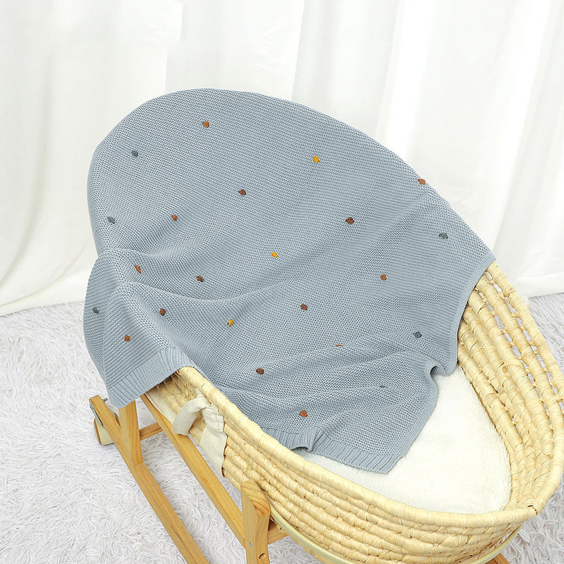 A cozy knitted solid color baby blanket featuring hand-embroidered pom poms, available in white, pink, blue, and khaki.