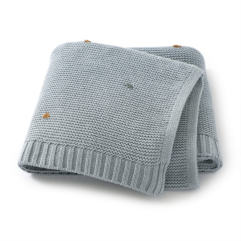 A cozy knitted solid color baby blanket featuring hand-embroidered pom poms, available in white, pink, blue, and khaki.