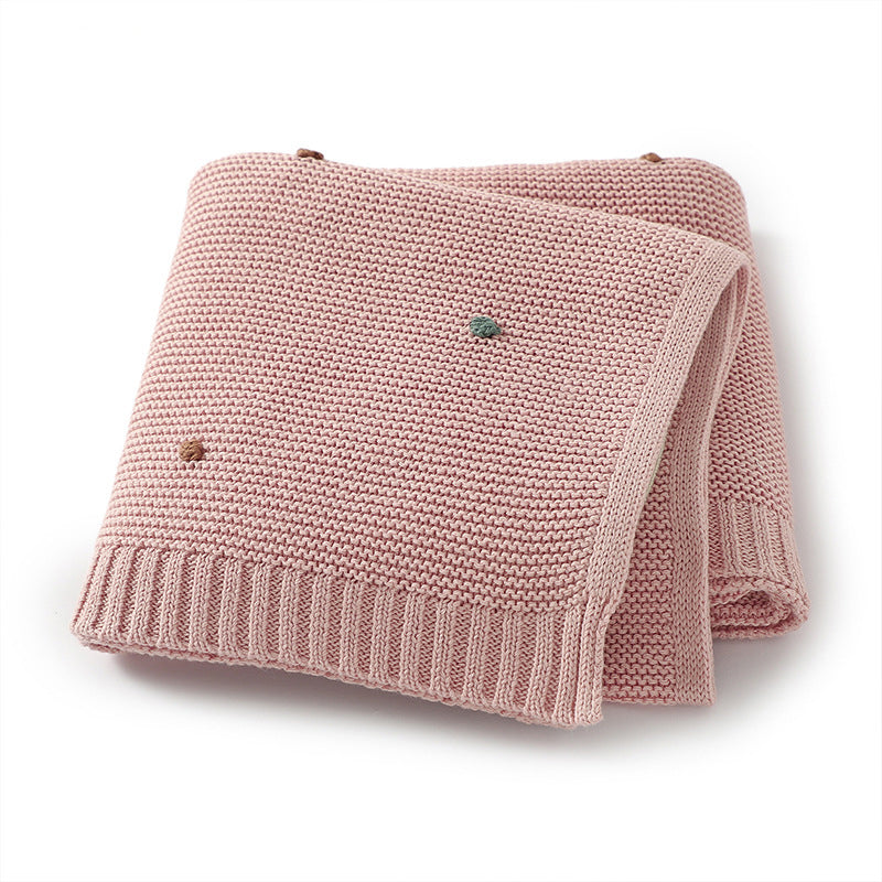 A cozy knitted solid color baby blanket featuring hand-embroidered pom poms, available in white, pink, blue, and khaki.