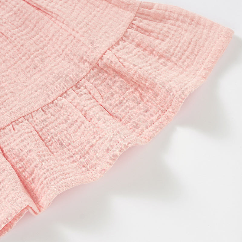 A soft and stylish Organic Cotton Muslin Baby Dress in three colors, featuring button straps and textured fabric, perfect for babies.