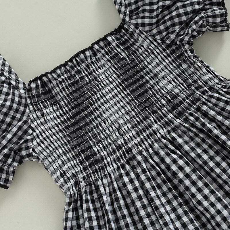 A stylish black plaid smocked dress featuring puff sleeves and a ruffle hem, perfect for girls' special occasions and everyday wear.