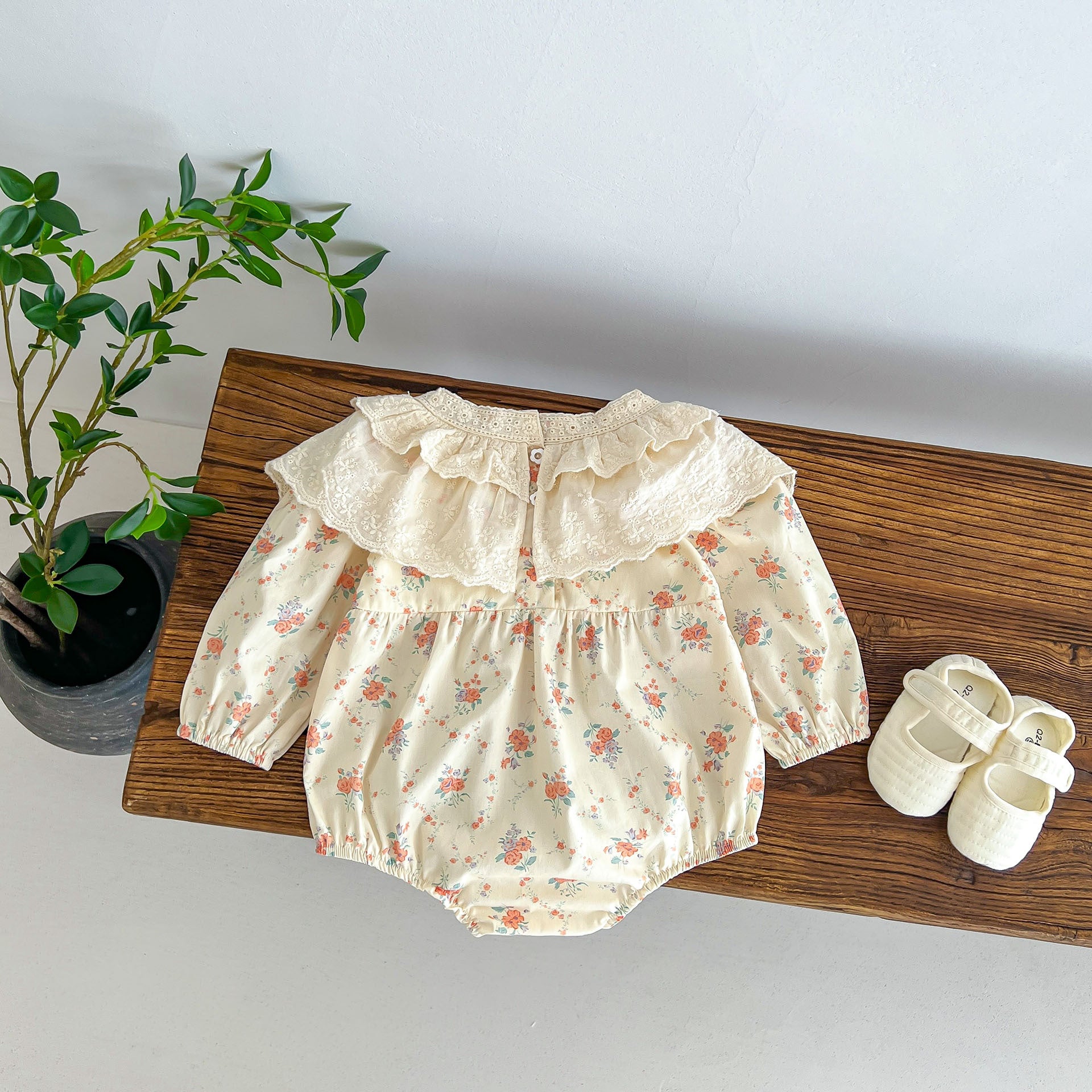 A cute baby girl wearing a long sleeve princess onesie with floral and solid patterns in white and pink colors.