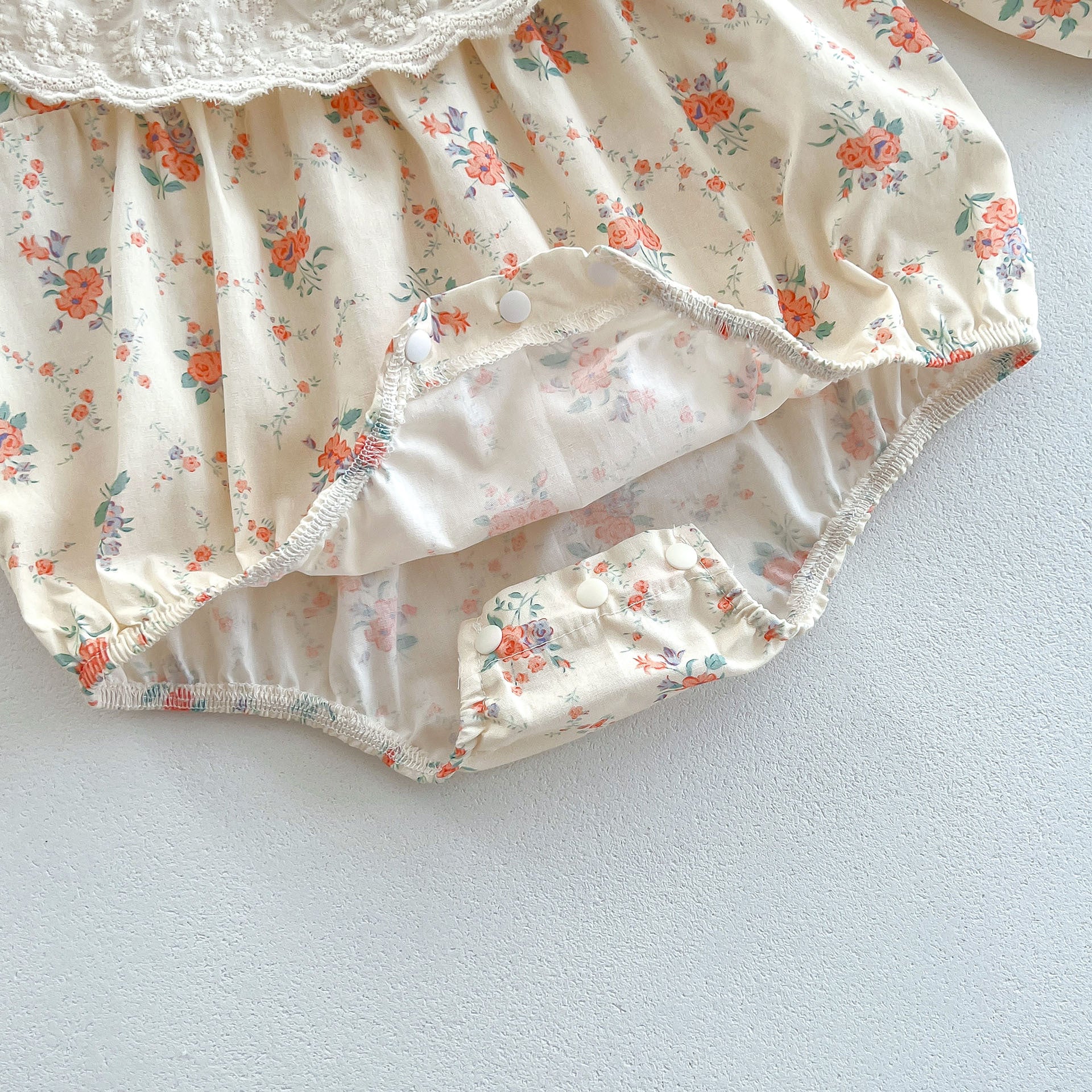 A cute baby girl wearing a long sleeve princess onesie with floral and solid patterns in white and pink colors.