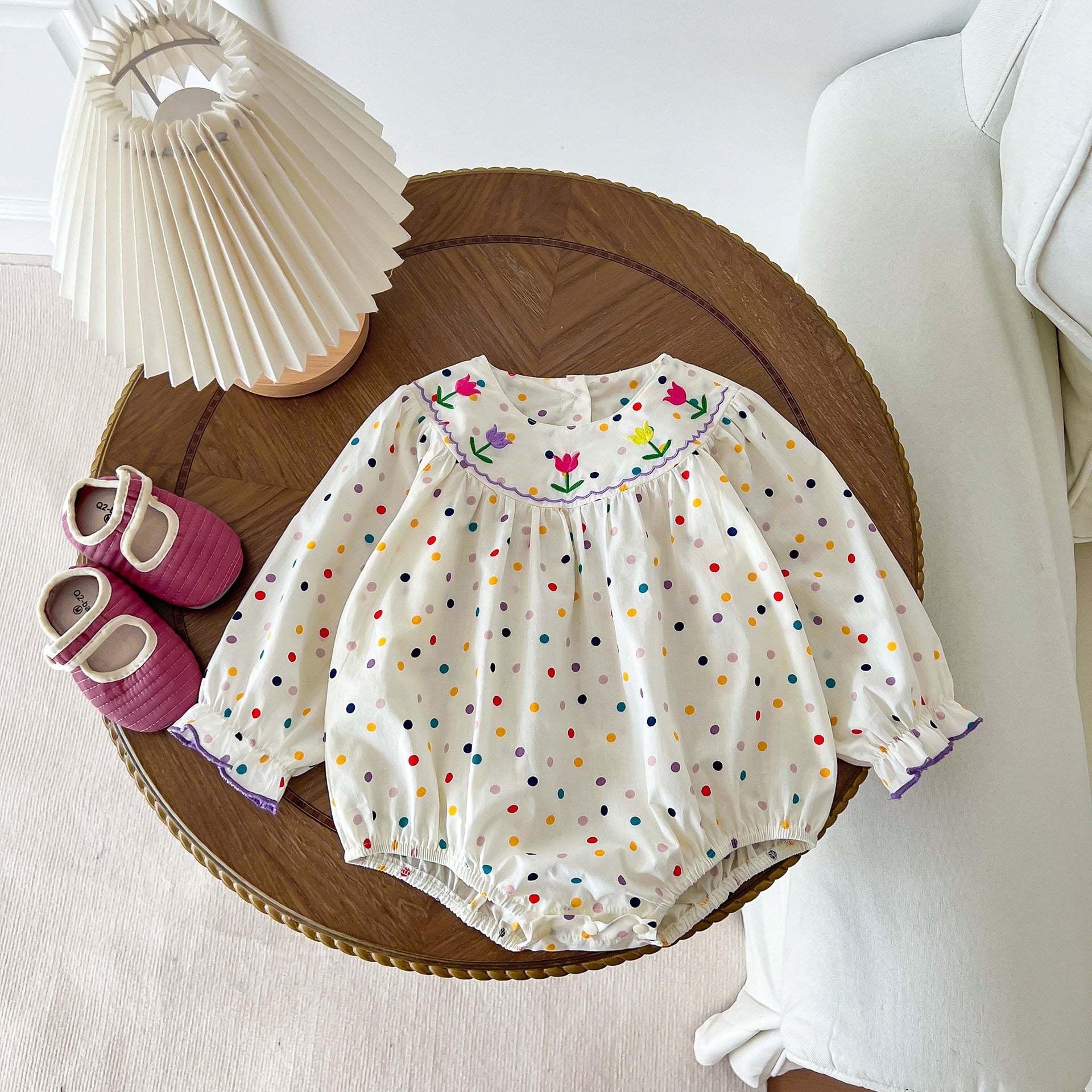 A cute baby girl wearing a long sleeve princess onesie with floral and solid patterns in white and pink colors.