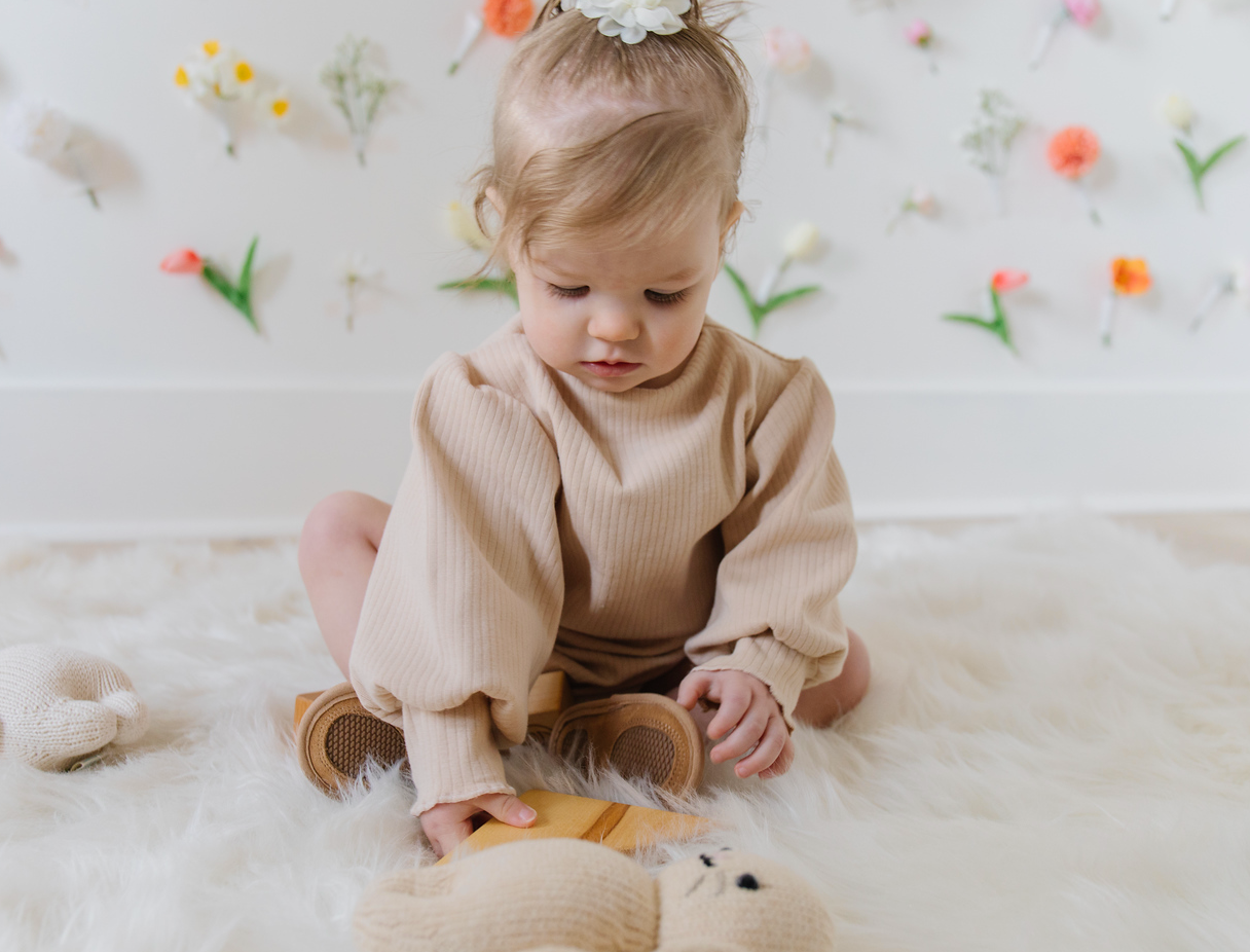 A soft ribbed baby bodysuit in green, ecru, and beige colors, showcasing its gentle fabric and stylish design.