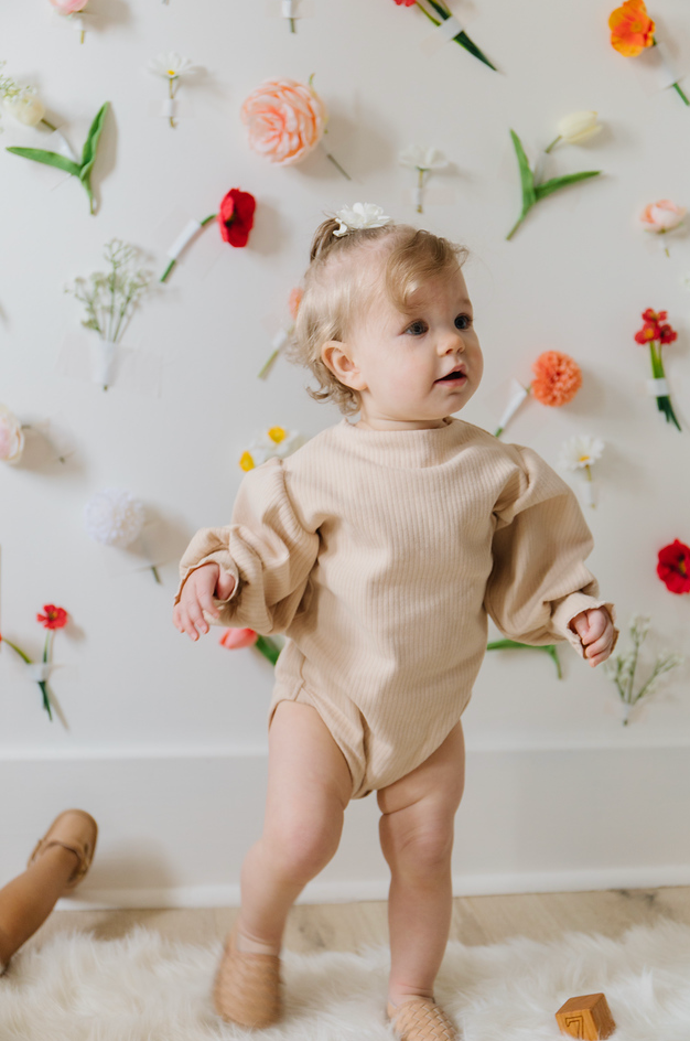A soft ribbed baby bodysuit in green, ecru, and beige colors, showcasing its gentle fabric and stylish design.
