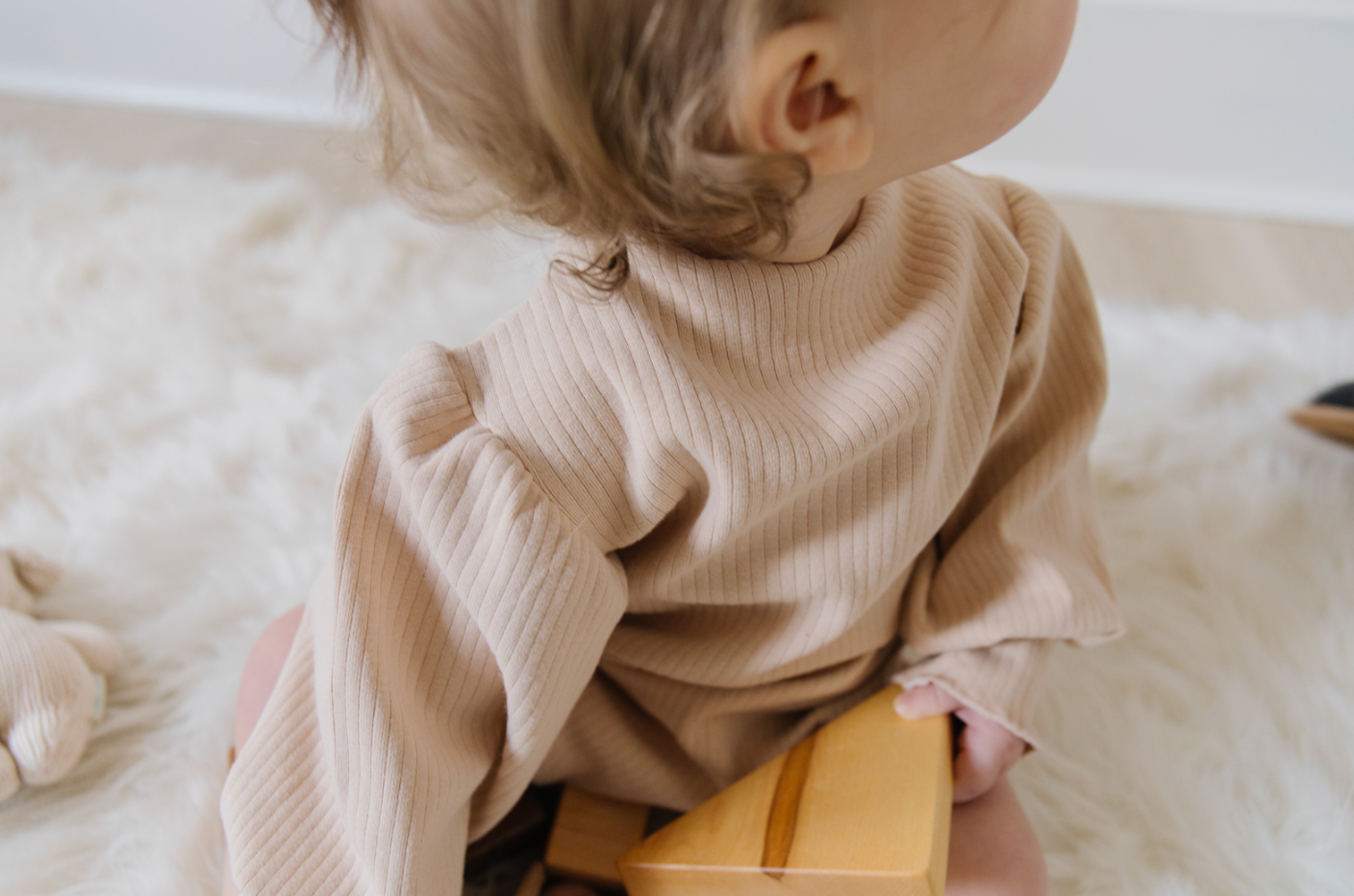 A soft ribbed baby bodysuit in green, ecru, and beige colors, showcasing its gentle fabric and stylish design.