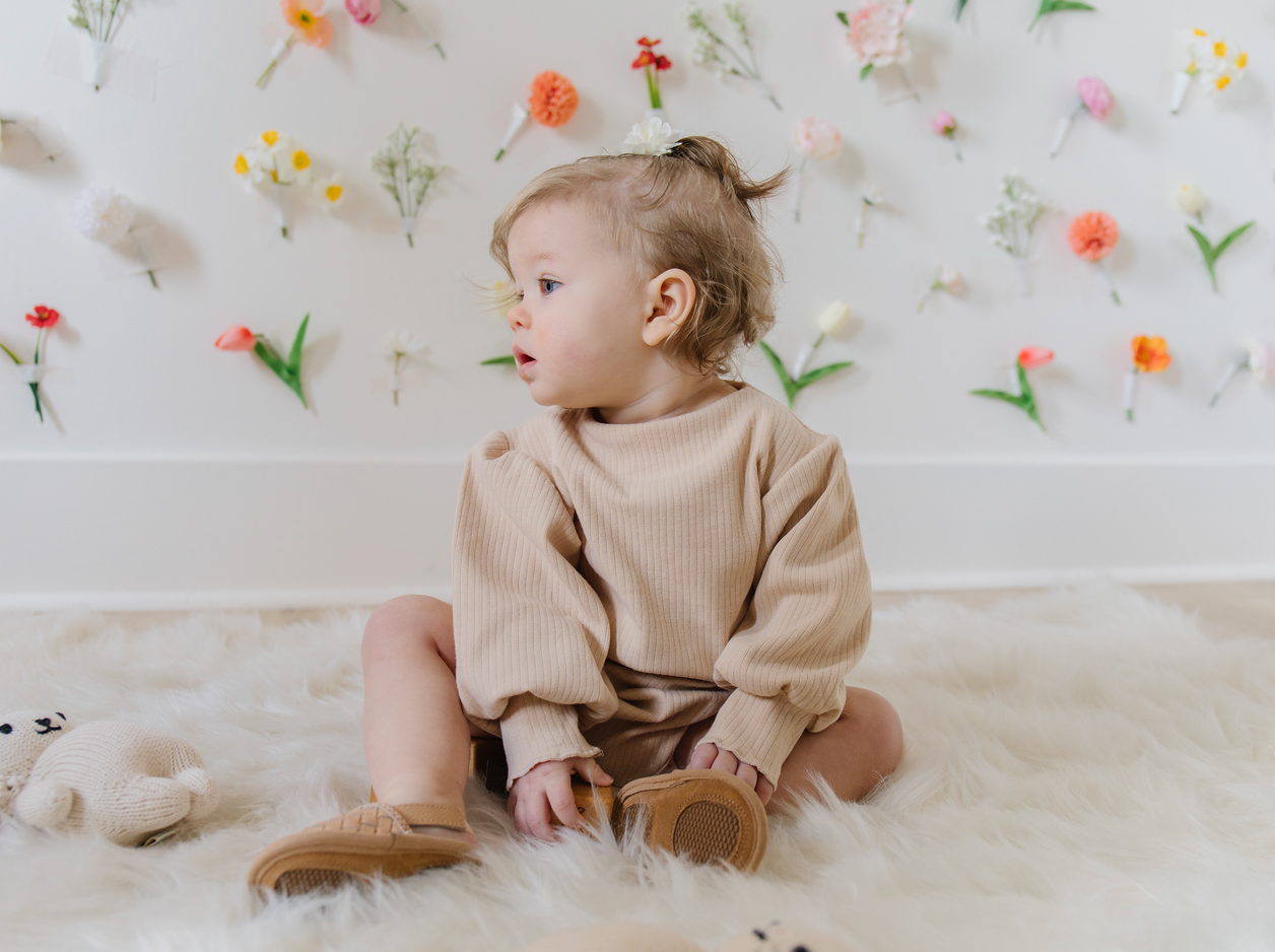 A soft ribbed baby bodysuit in green, ecru, and beige colors, showcasing its gentle fabric and stylish design.