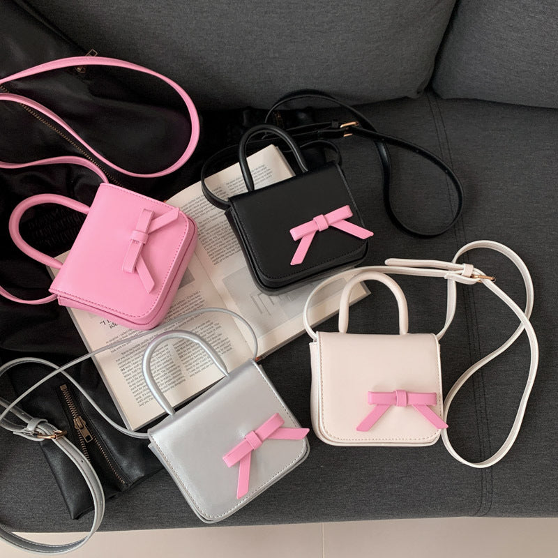 Stylish Creative Carry-On Girls’ Portable Mini Bow Princess Crossbody bag in white, black, pink, and silver colors with a cute bow design.