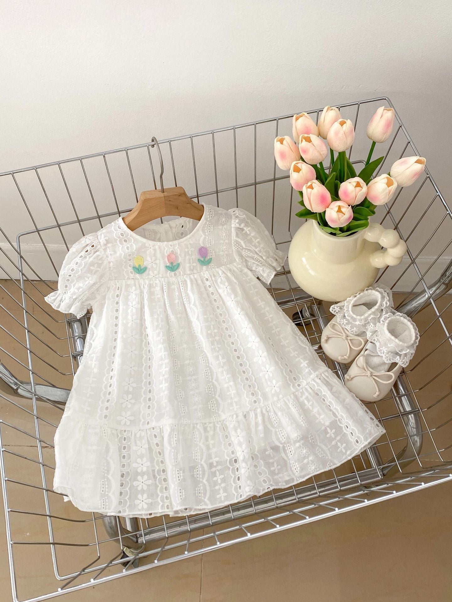 A cute summer dress for baby girls featuring floral embroidery and hollow-out short sleeves, made from soft cotton in white color.