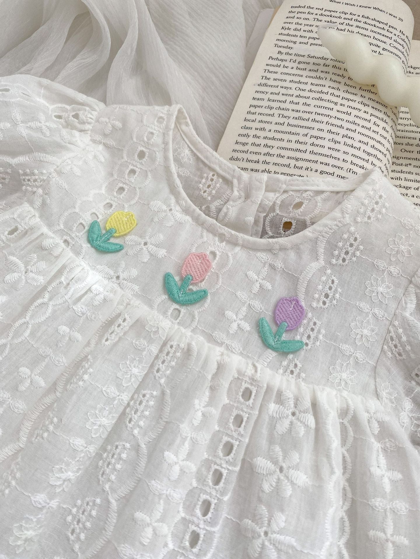 A cute summer dress for baby girls featuring floral embroidery and hollow-out short sleeves, made from soft cotton in white color.
