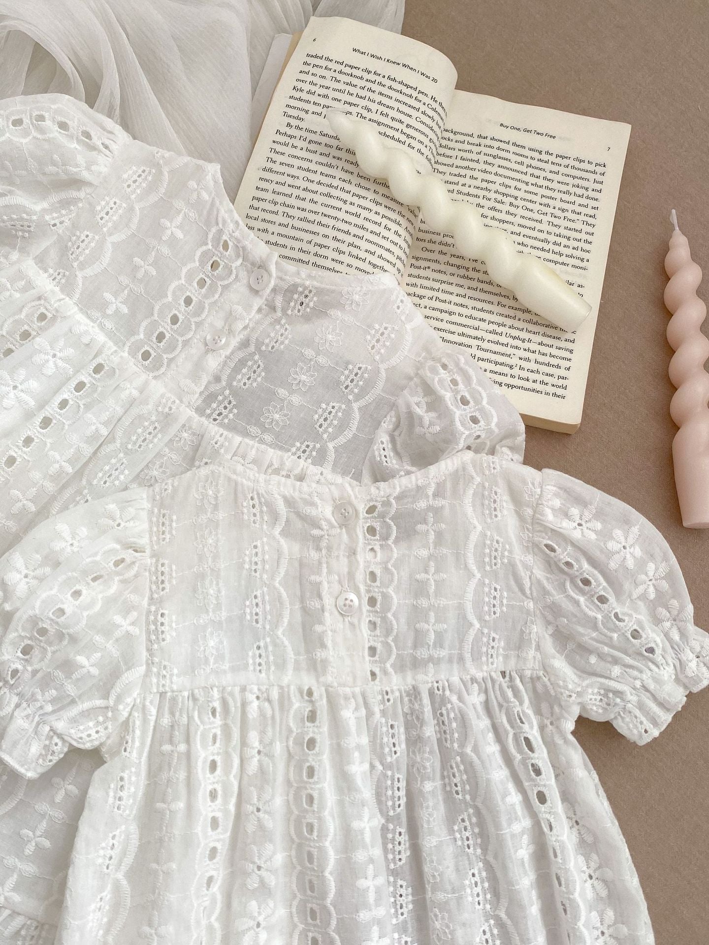A cute summer dress for baby girls featuring floral embroidery and hollow-out short sleeves, made from soft cotton in white color.