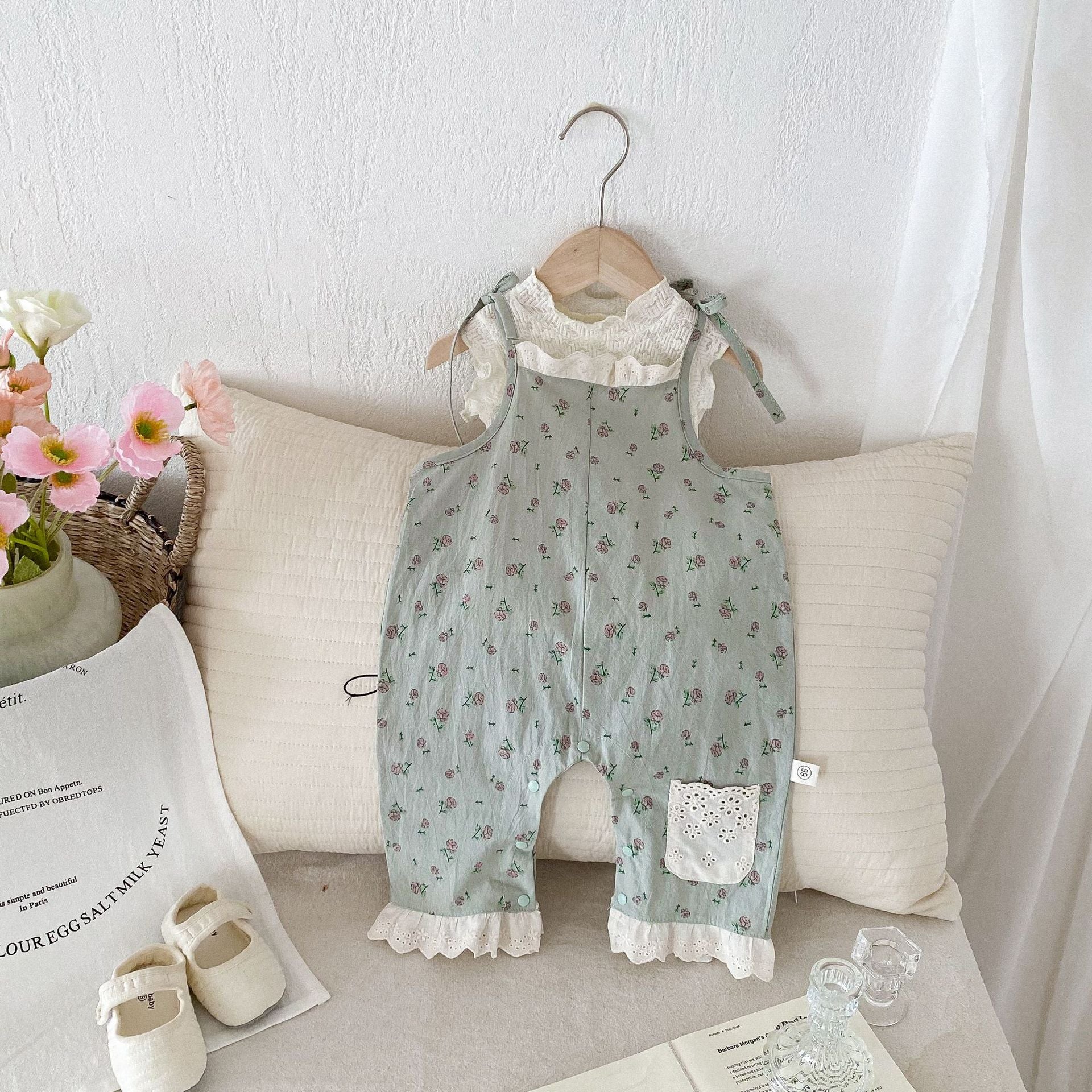 A cute baby girl wearing a green sleeveless floral pattern strap romper, perfect for summer outings.
