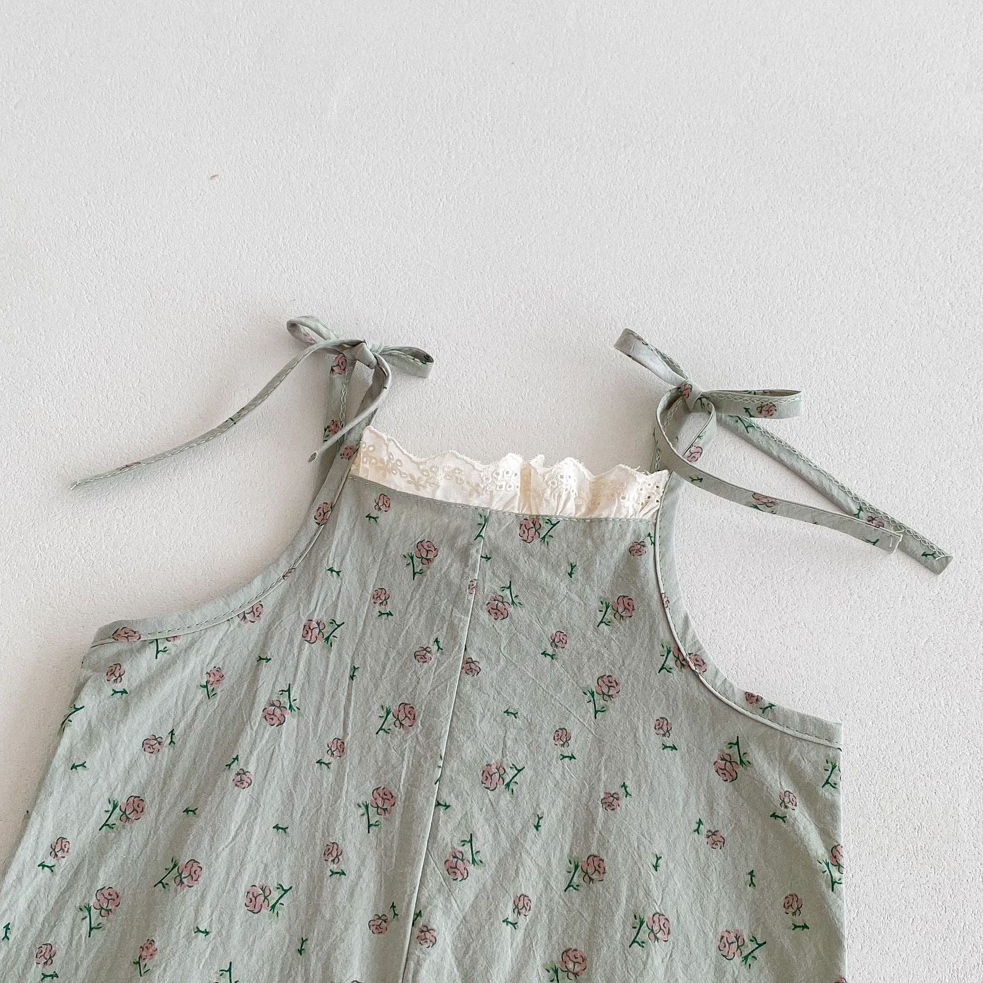 A cute baby girl wearing a green sleeveless floral pattern strap romper, perfect for summer outings.